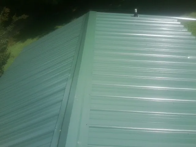 New green metal panels meeting at the ridge of a roof — Flat Roof Repair work by our crew in Midway